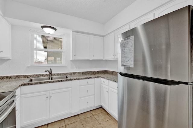 kitchen featuring a textured ceiling, light tile patterned floors, stainless steel appliances, a sink, and white cabinets