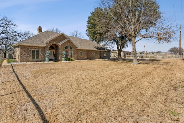 view of front facade featuring brick siding, a chimney, a shingled roof, and fence