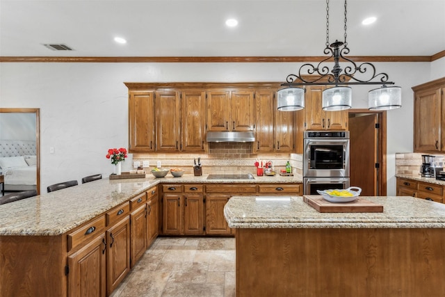 kitchen featuring crown molding, double oven, brown cabinetry, under cabinet range hood, and black electric cooktop