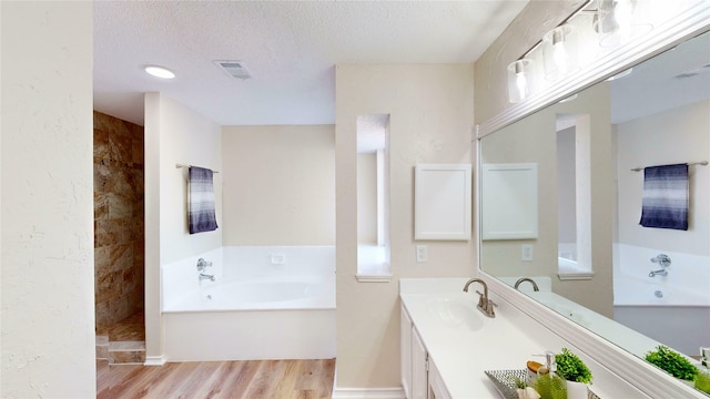 full bath featuring a textured ceiling, wood finished floors, a sink, visible vents, and a bath