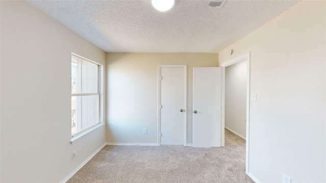 unfurnished bedroom featuring a textured ceiling, carpet floors, visible vents, and baseboards