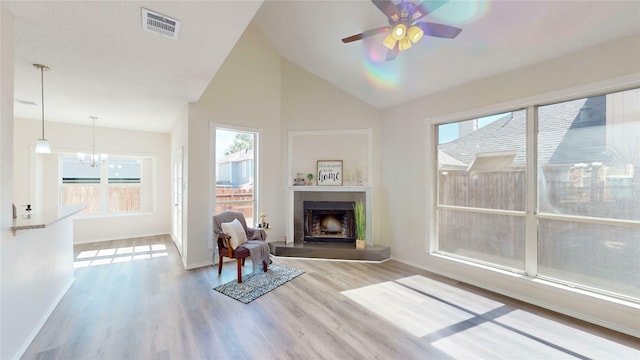 unfurnished room with a fireplace with raised hearth, ceiling fan with notable chandelier, wood finished floors, visible vents, and baseboards