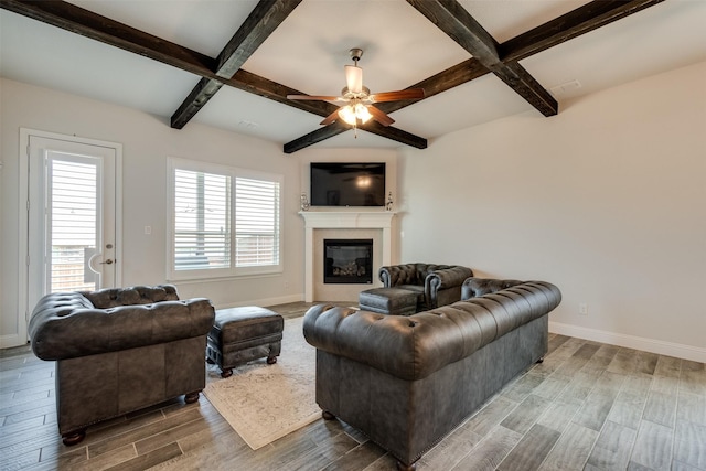 living area featuring baseboards, a glass covered fireplace, beamed ceiling, and wood finish floors