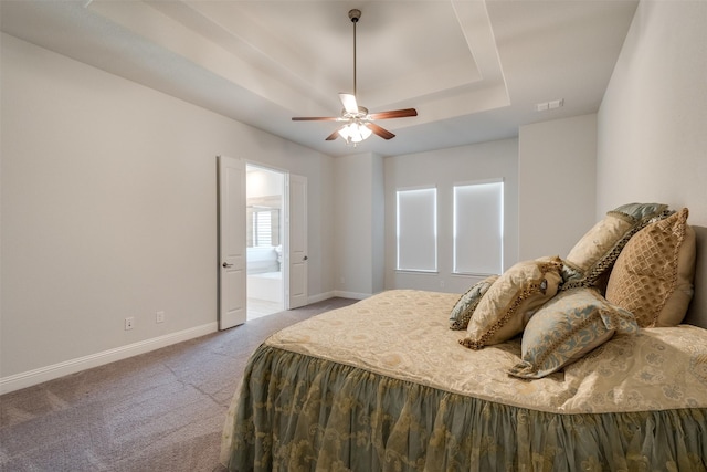 carpeted bedroom featuring a tray ceiling, visible vents, ceiling fan, ensuite bath, and baseboards