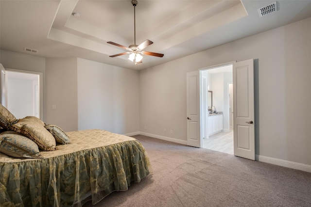 bedroom featuring a raised ceiling, light colored carpet, visible vents, and baseboards