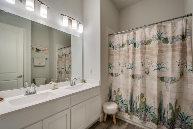 bathroom with wood finished floors, a sink, toilet, and double vanity