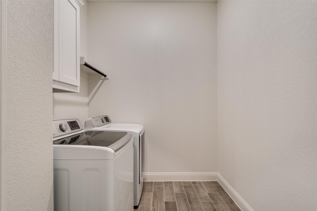 laundry area featuring wood tiled floor, baseboards, cabinet space, and washing machine and clothes dryer