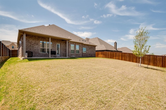 rear view of property with a yard, brick siding, and a fenced backyard