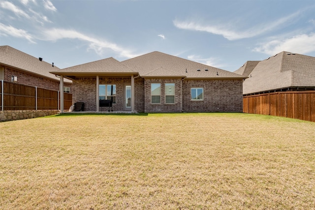 rear view of house featuring a yard, brick siding, and fence private yard