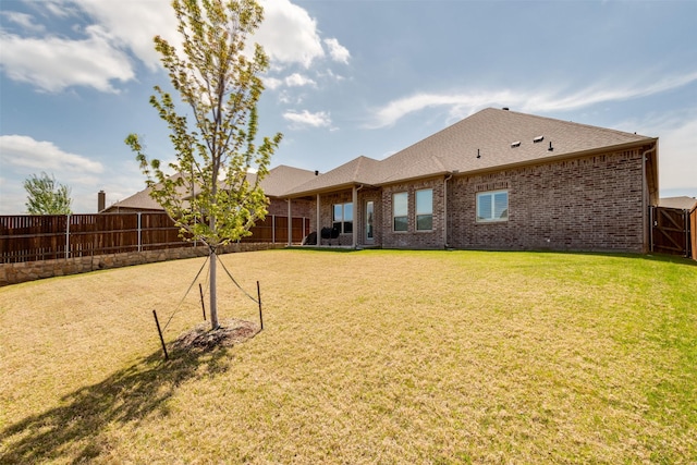 back of house featuring a shingled roof, brick siding, a lawn, and a fenced backyard