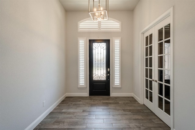 foyer with dark wood-type flooring, french doors, a notable chandelier, and baseboards