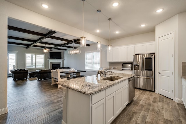 kitchen with an island with sink, dark wood-type flooring, stainless steel appliances, a fireplace, and a sink