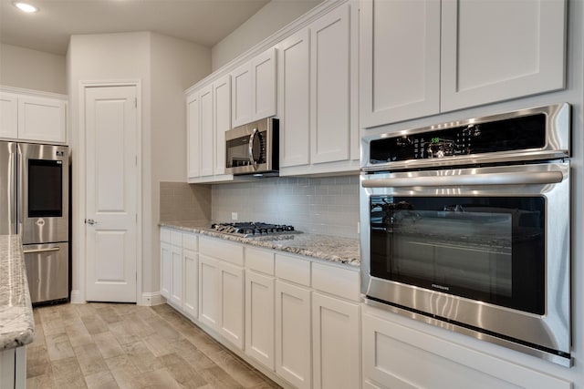 kitchen with light wood finished floors, tasteful backsplash, white cabinets, appliances with stainless steel finishes, and light stone countertops