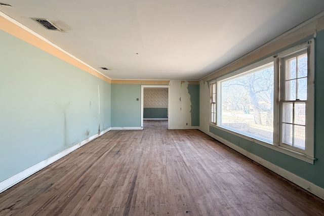 unfurnished room with baseboards, visible vents, wood finished floors, and ornamental molding