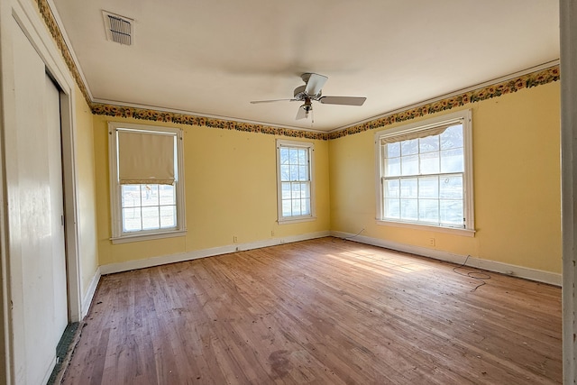 spare room with ornamental molding, light wood-type flooring, visible vents, and baseboards