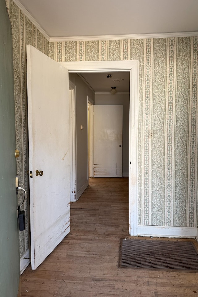 hallway with ornamental molding, wood finished floors, and wallpapered walls