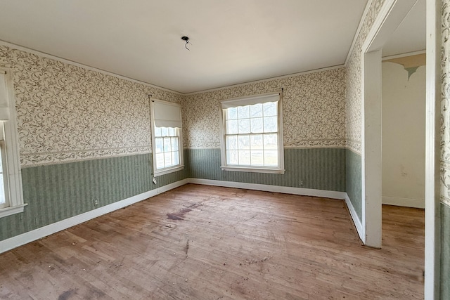 empty room with a wainscoted wall, wood finished floors, baseboards, wallpapered walls, and crown molding