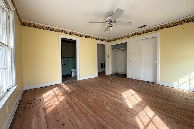 unfurnished bedroom featuring multiple closets, visible vents, ensuite bathroom, wood finished floors, and baseboards