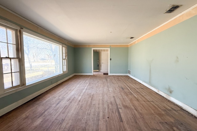 spare room featuring baseboards, visible vents, wood finished floors, and ornamental molding