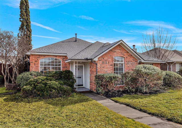 view of front of property with a shingled roof, a chimney, a front lawn, and brick siding