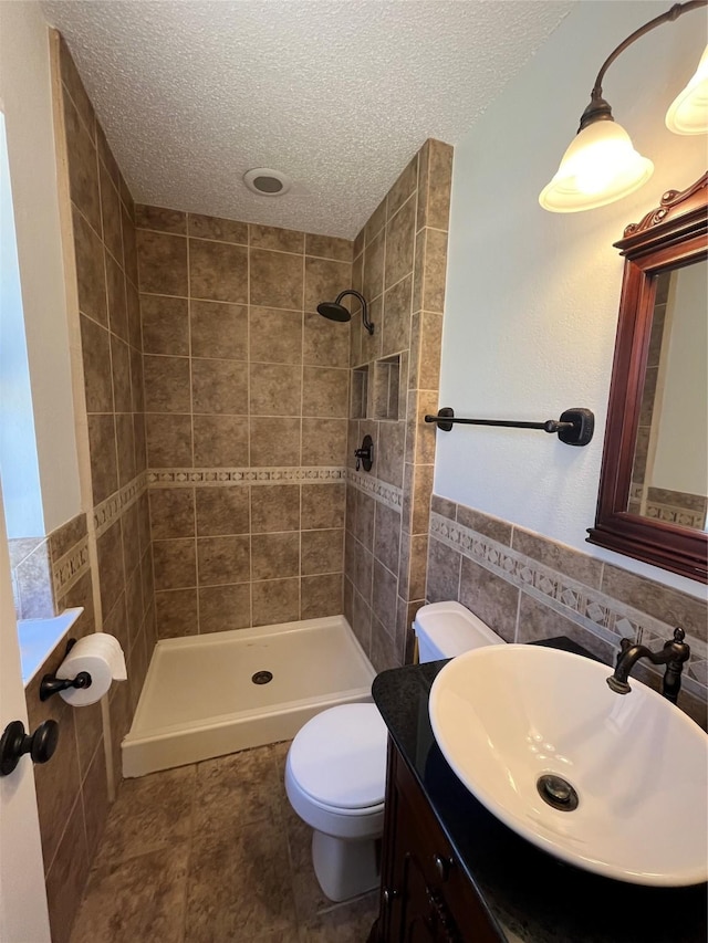 bathroom featuring toilet, a stall shower, a textured ceiling, and tile walls