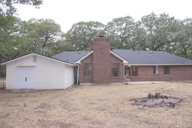 rear view of house featuring a shingled roof, a chimney, and brick siding