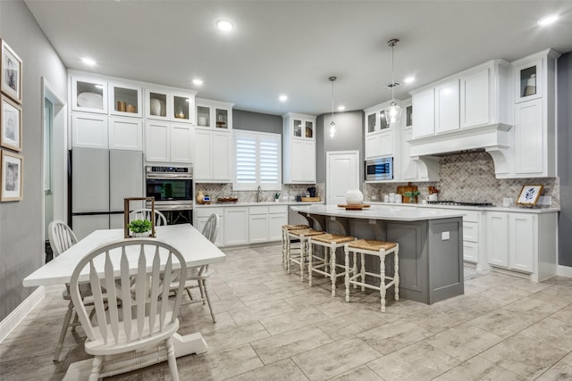 kitchen featuring a kitchen breakfast bar, a center island, built in appliances, white cabinetry, and a sink