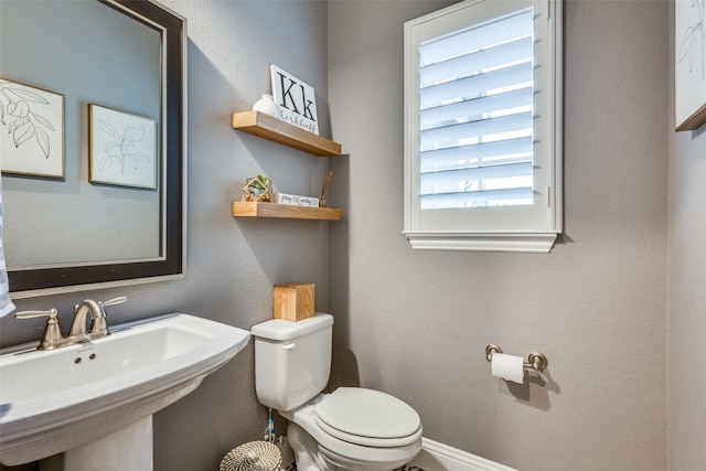 half bathroom featuring a textured wall, baseboards, a sink, and toilet