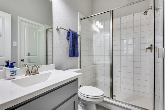 bathroom with toilet, a shower stall, vanity, and a textured wall