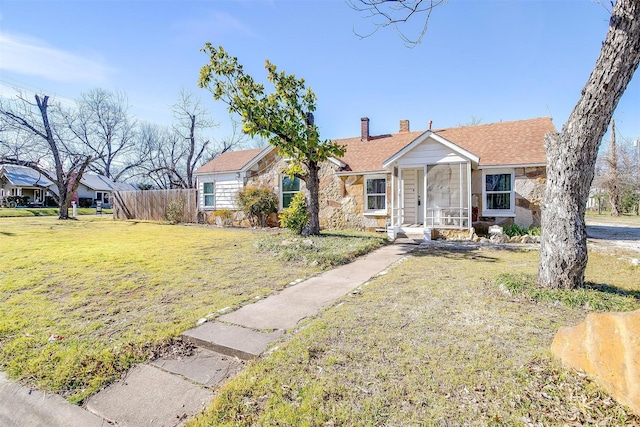 view of front facade with a front yard, stone siding, fence, and a chimney