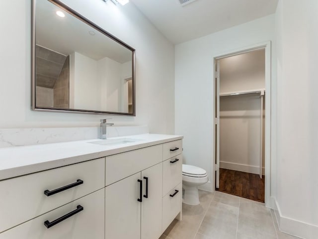 bathroom featuring toilet, visible vents, vanity, baseboards, and a spacious closet