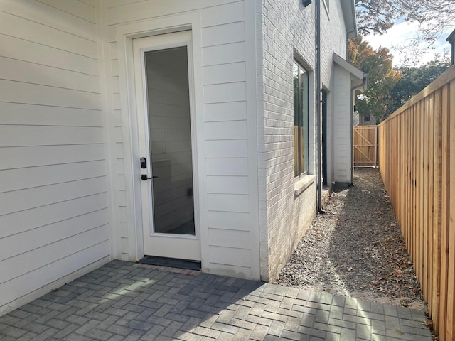 property entrance featuring a patio area, fence, and brick siding