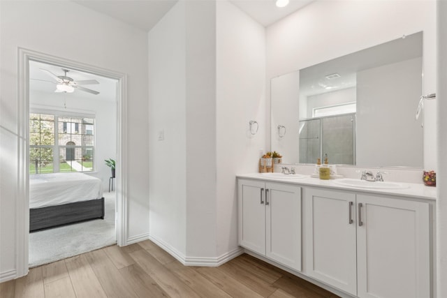 ensuite bathroom featuring double vanity, a stall shower, a sink, wood finished floors, and baseboards