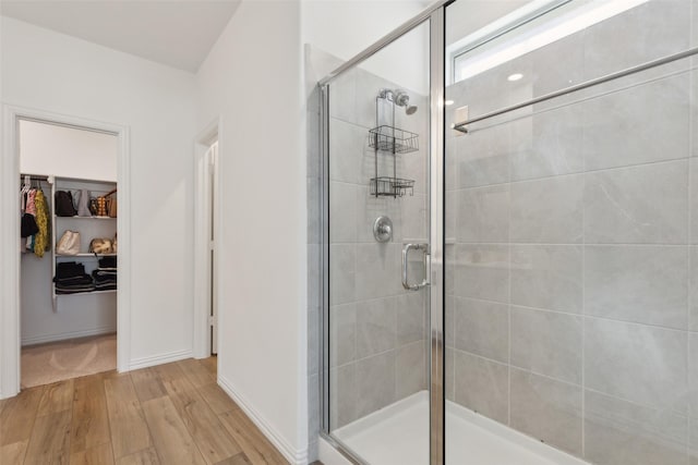 full bath featuring a spacious closet, wood finished floors, a shower stall, and baseboards