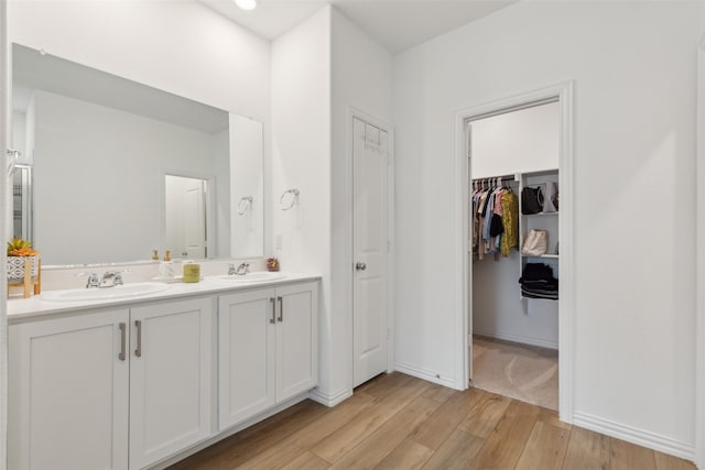 full bathroom with double vanity, wood finished floors, a spacious closet, and a sink