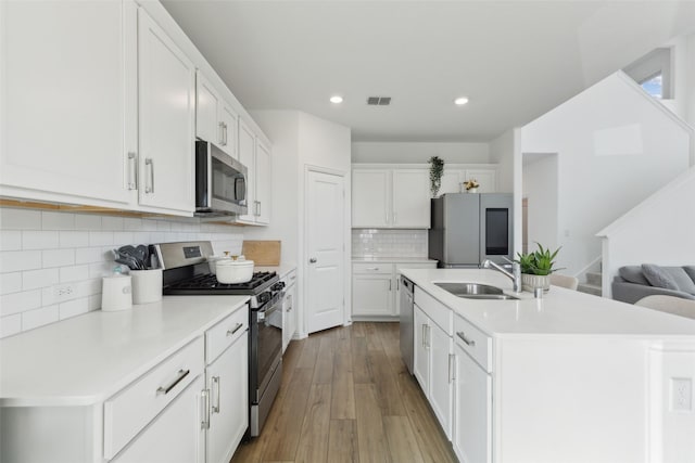 kitchen with stainless steel appliances, a sink, visible vents, white cabinets, and a center island with sink