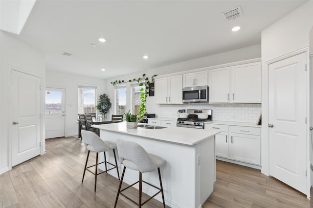 kitchen with stainless steel appliances, visible vents, backsplash, a sink, and an island with sink