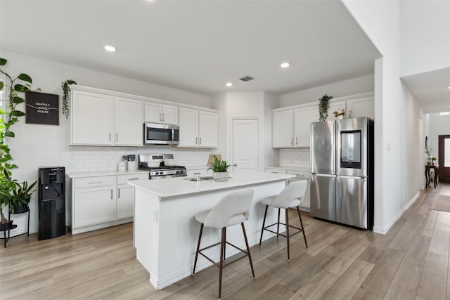 kitchen with appliances with stainless steel finishes, light wood-style floors, a center island with sink, and white cabinets