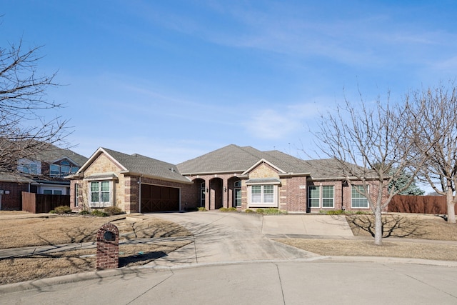 view of front of house featuring an attached garage, fence, brick siding, and driveway