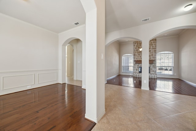 unfurnished room featuring visible vents, ornamental molding, a stone fireplace, and wood finished floors