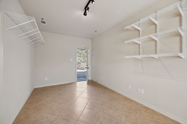 tiled empty room featuring baseboards, visible vents, and track lighting