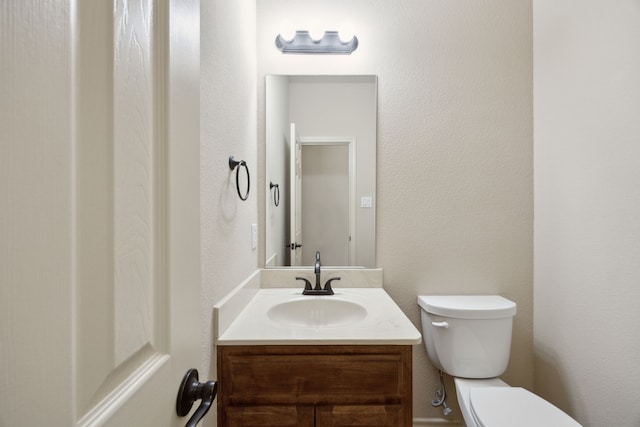 bathroom featuring a textured wall, vanity, and toilet