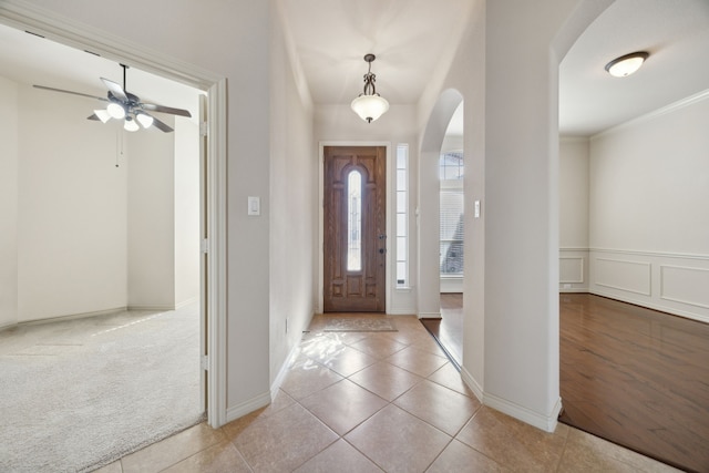 tiled entrance foyer with arched walkways, a decorative wall, a wainscoted wall, carpet, and crown molding