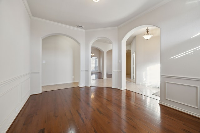 unfurnished room with visible vents, crown molding, a decorative wall, and hardwood / wood-style flooring