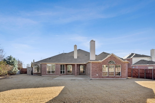 back of house with a fenced backyard, brick siding, roof with shingles, a chimney, and a patio area