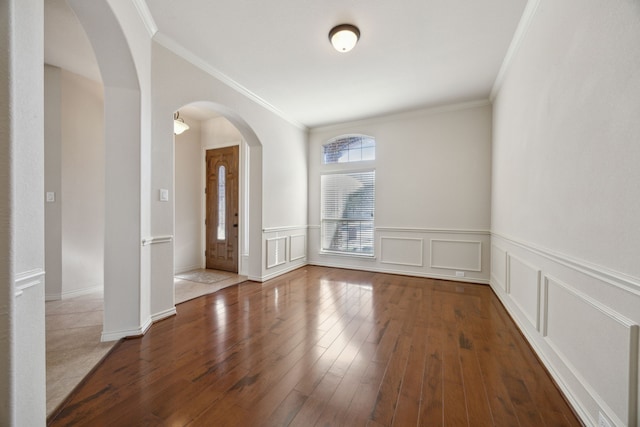 spare room with arched walkways, crown molding, a decorative wall, and hardwood / wood-style flooring