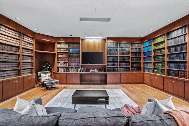 living room featuring built in features, bookshelves, wood walls, and wood finished floors