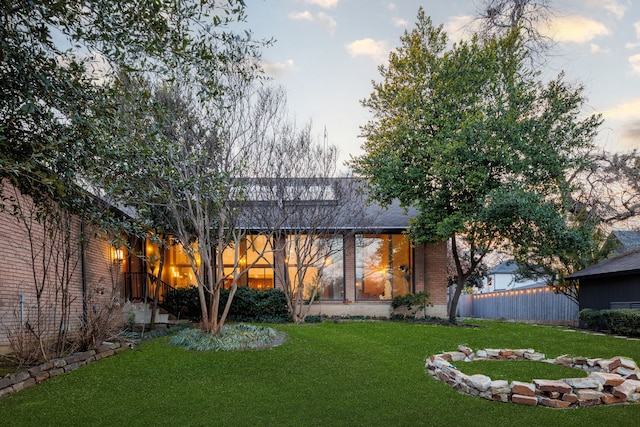 back of property at dusk featuring brick siding, a lawn, and fence