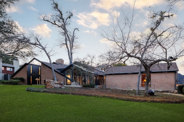 rear view of property featuring brick siding, a chimney, and a yard