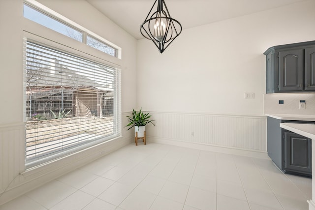 unfurnished dining area with a notable chandelier, a wainscoted wall, and light tile patterned flooring